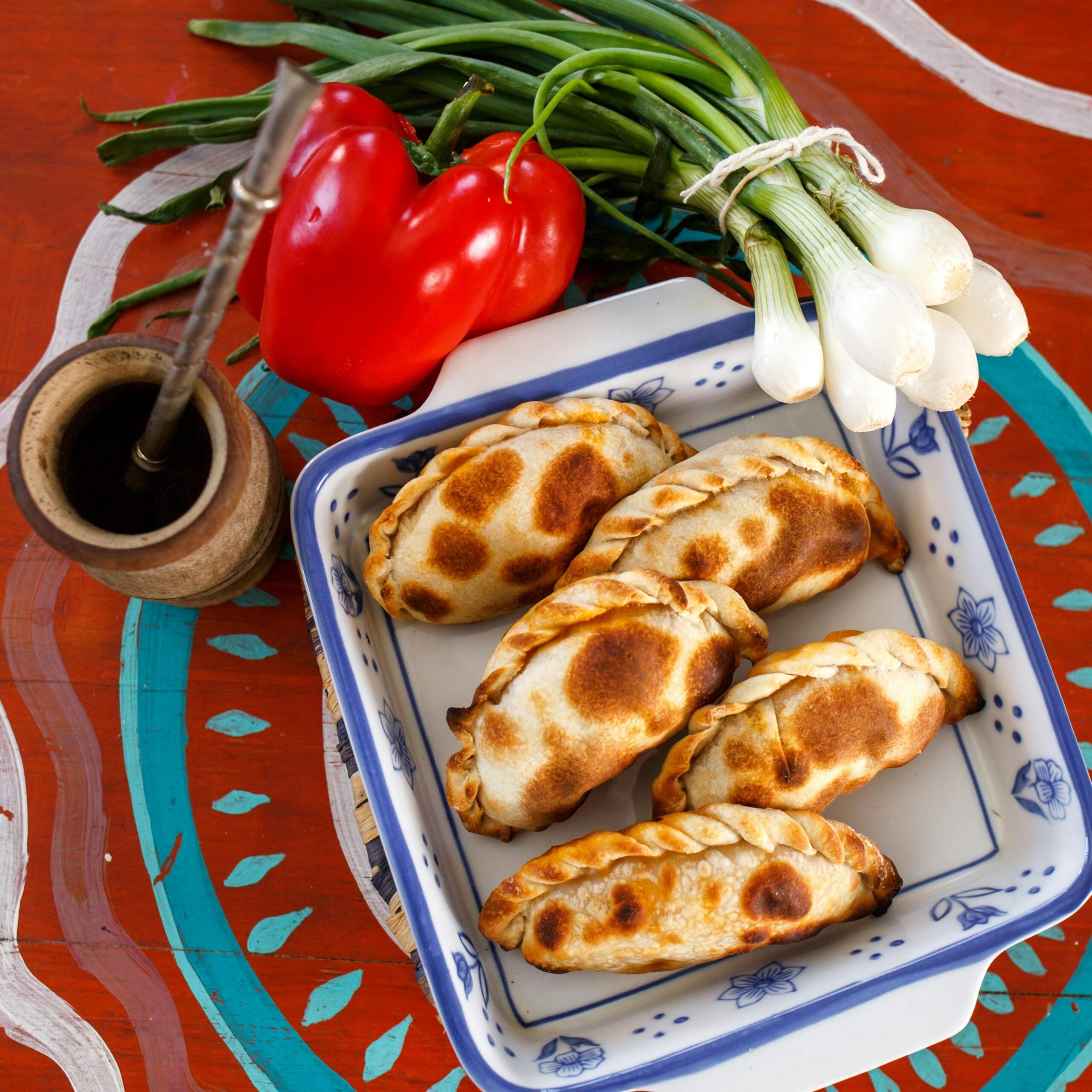 Plate of Argentine empanadas with traditional mate, red pepper, and green onions.